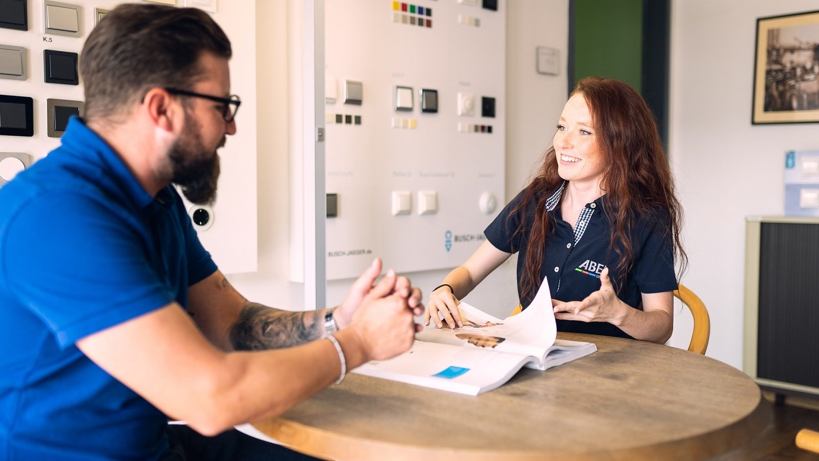 Woman explains to a man over a brochure at a table, switches on display.