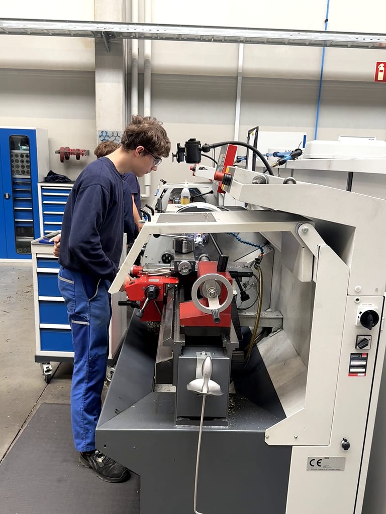 Student in safety glasses operating a metalworking machine in a workshop.