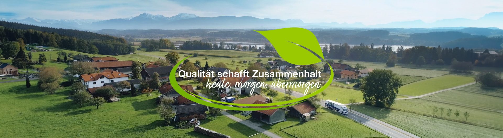 Aerial view of an alpine village, green fields, lake, and mountains, with 'Quality creates cohesion' text.