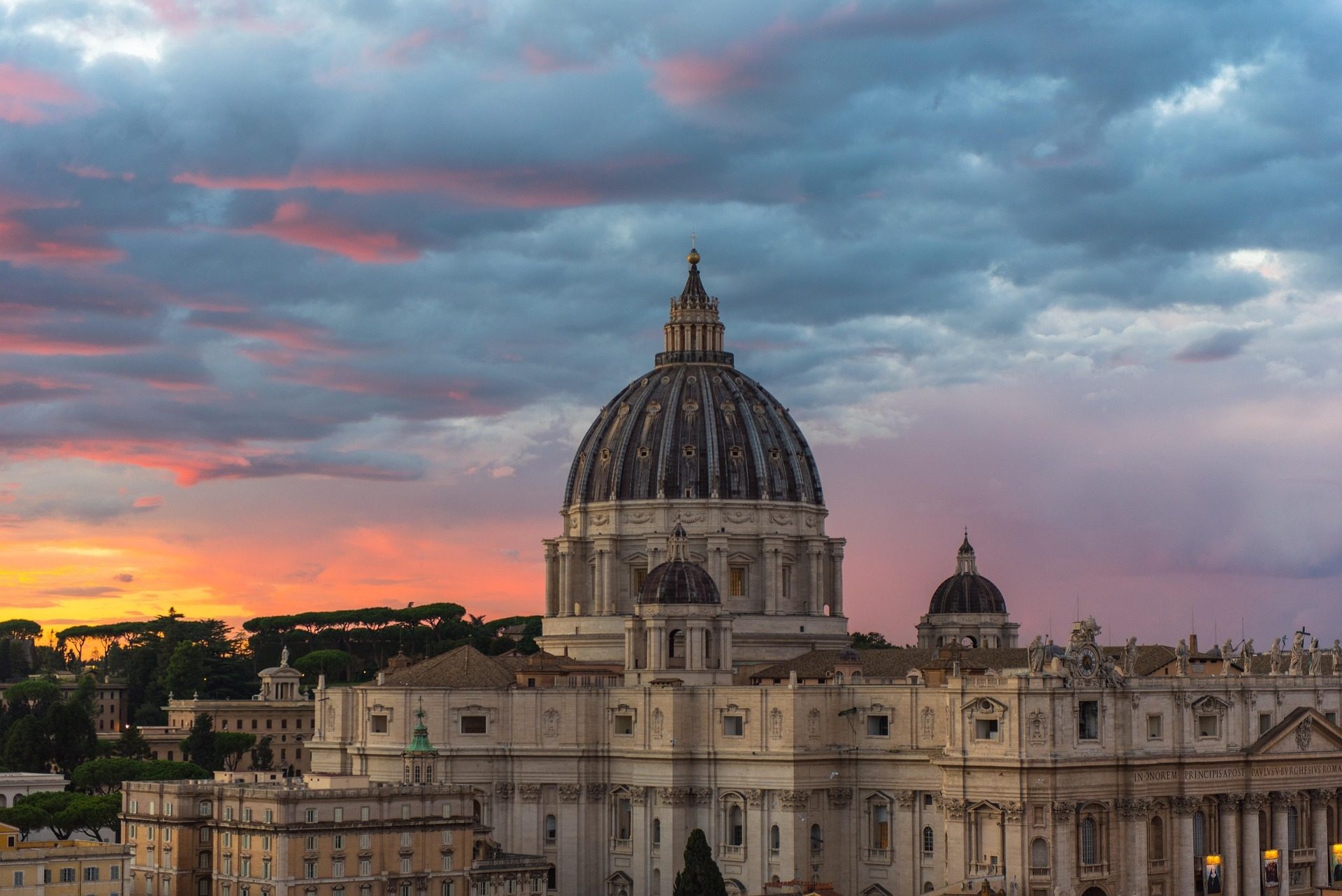 St. Peter's Basilica dome at sunset with pink and orange clouds.