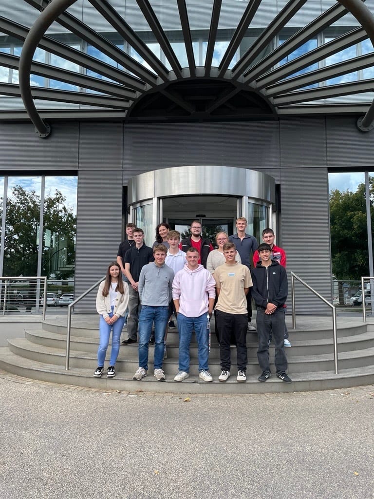 A group of young people standing on steps in front of a modern building with a glass canopy.