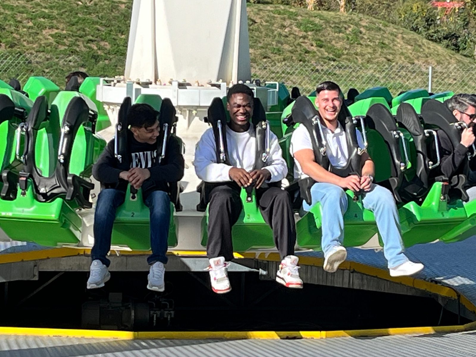 Three smiling men on a green amusement park ride with harnesses.