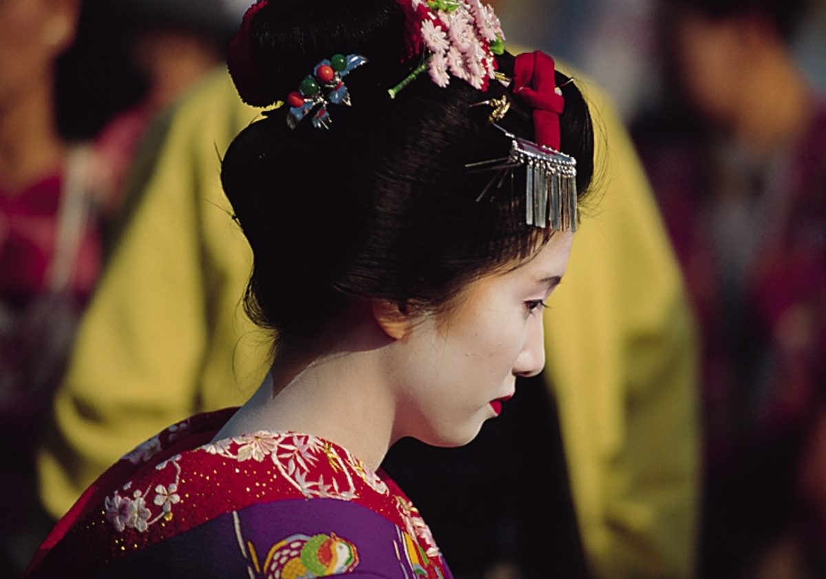 Japanese woman with traditional makeup, elaborate hair bun, kanzashi, and a colorful kimono.