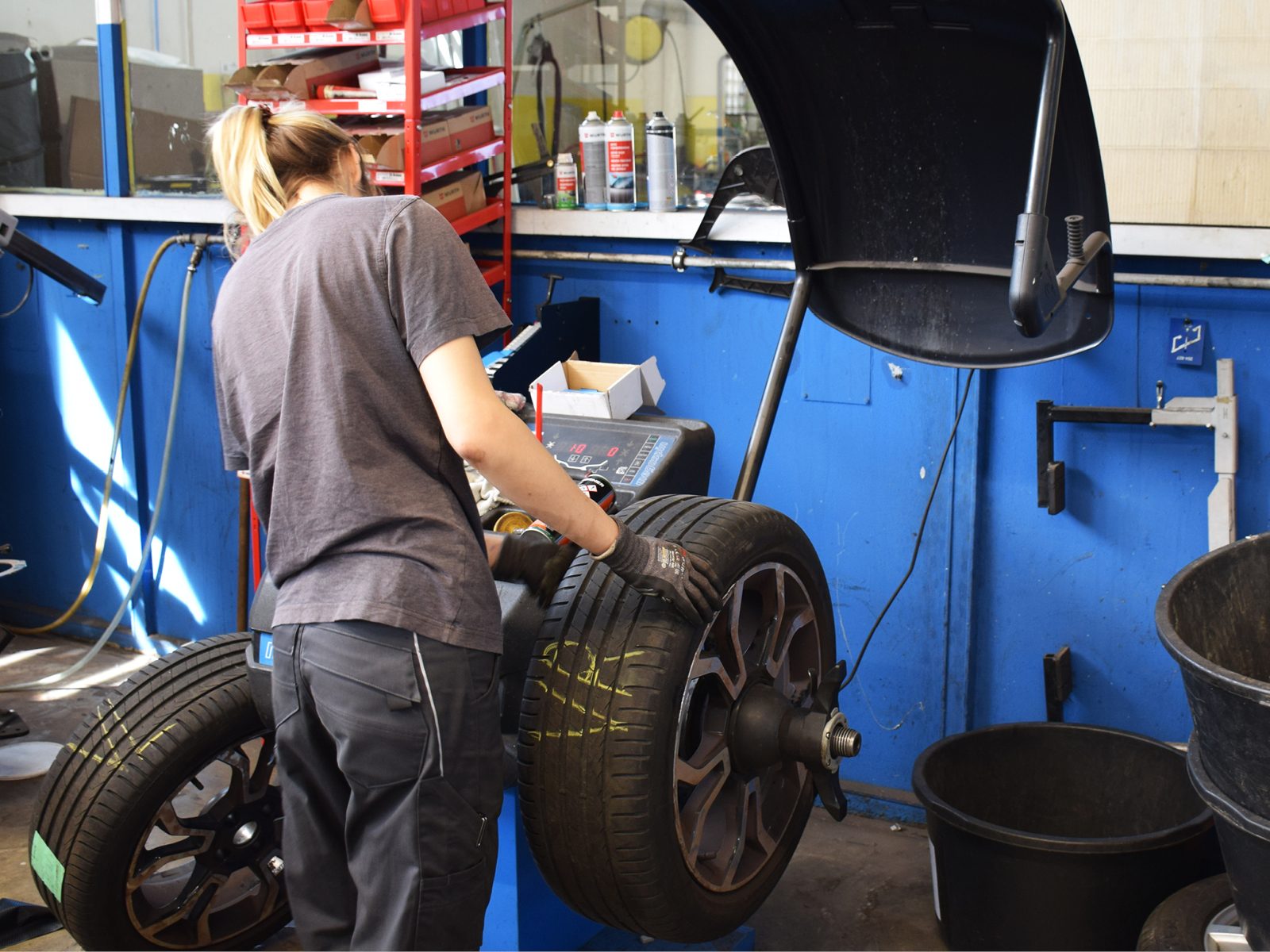 Worker balancing a car tire on a machine in a garage, viewed from behind.