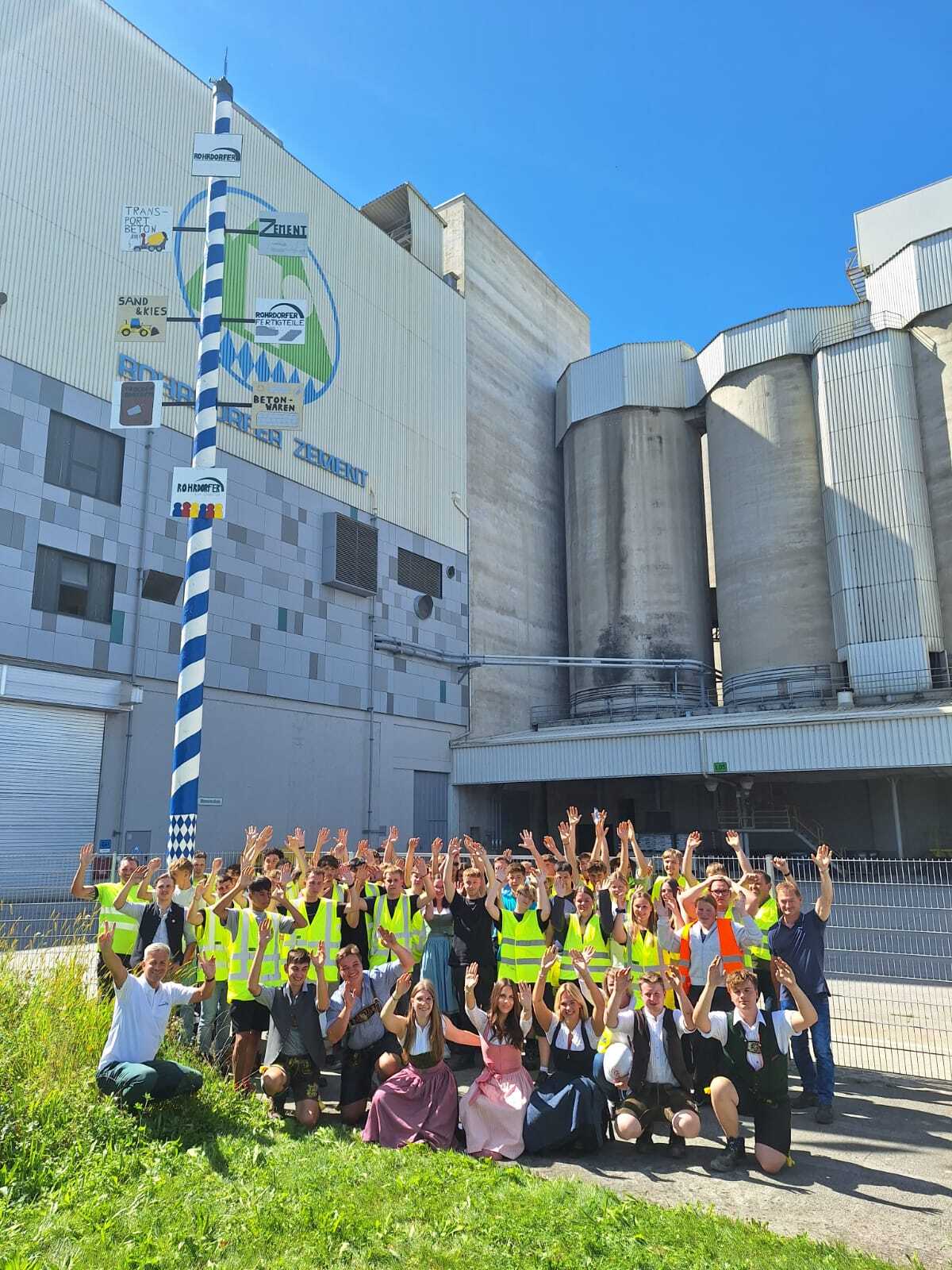 Group in safety vests and Bavarian dress waving at a cement factory with a Maypole.