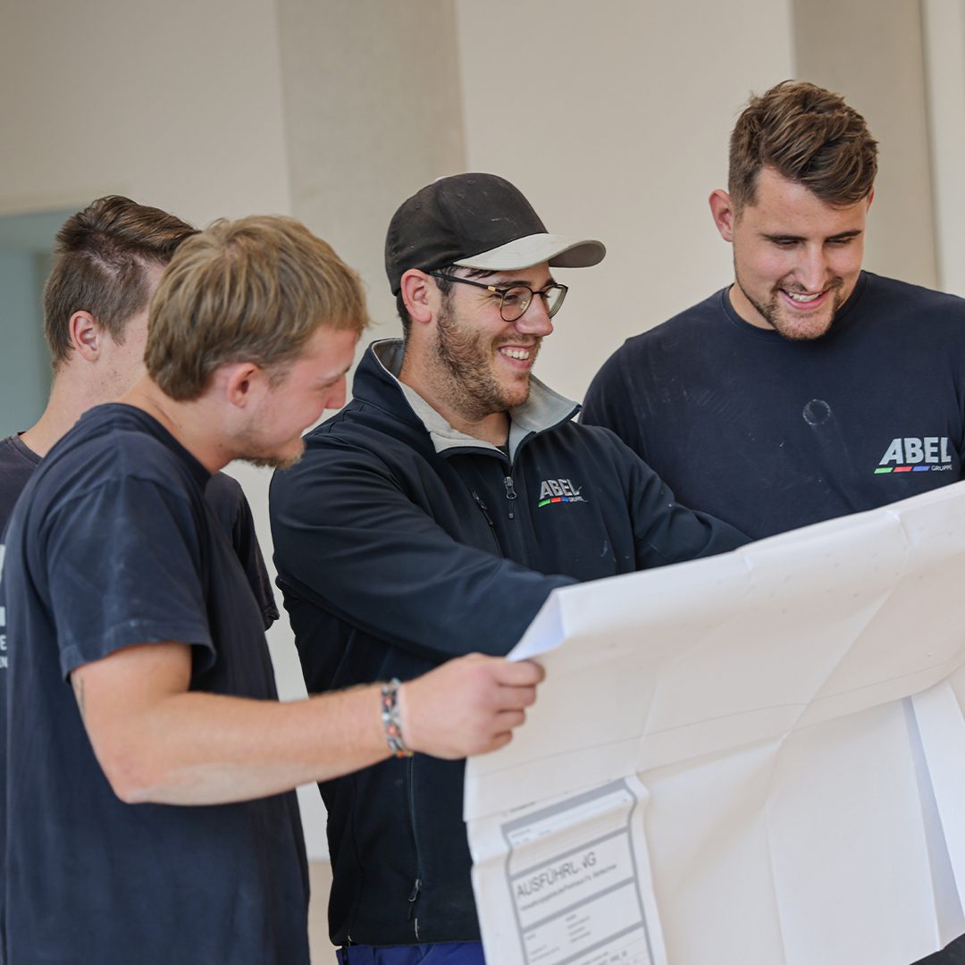 Four smiling men review construction blueprints together.