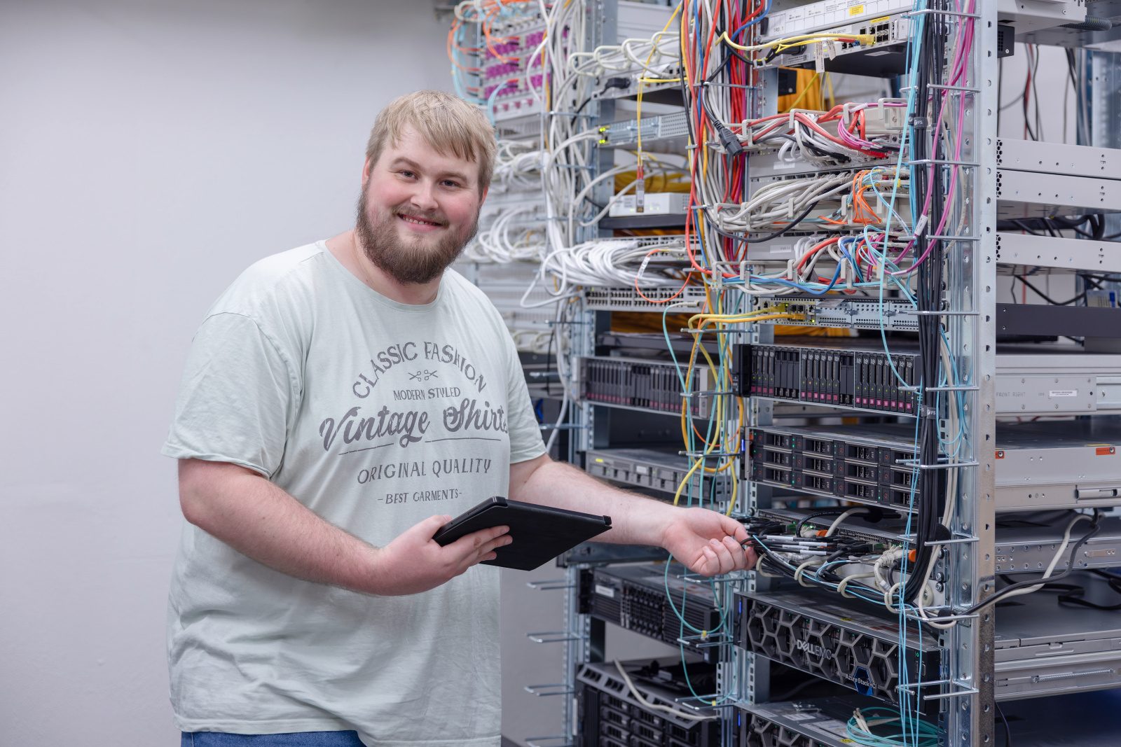 Smiling man with tablet managing server rack cables.