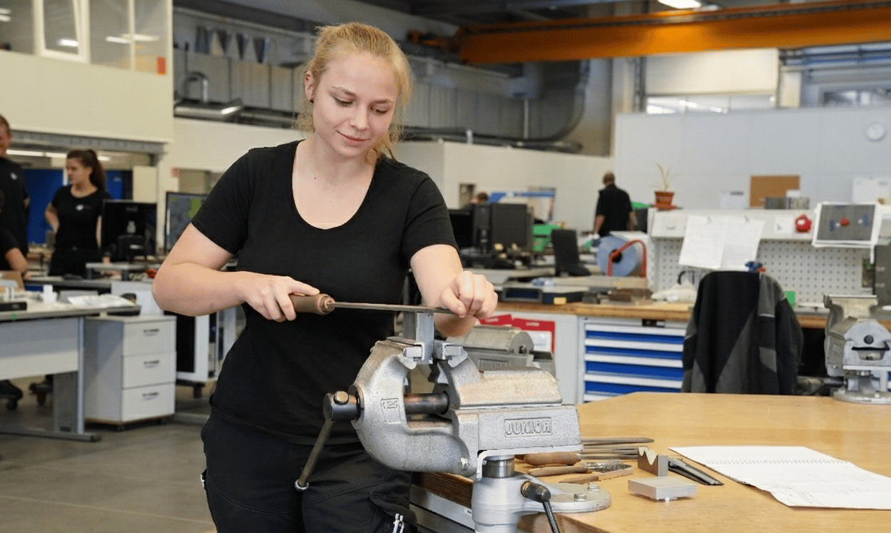 Woman filing metal in a vise in a workshop.