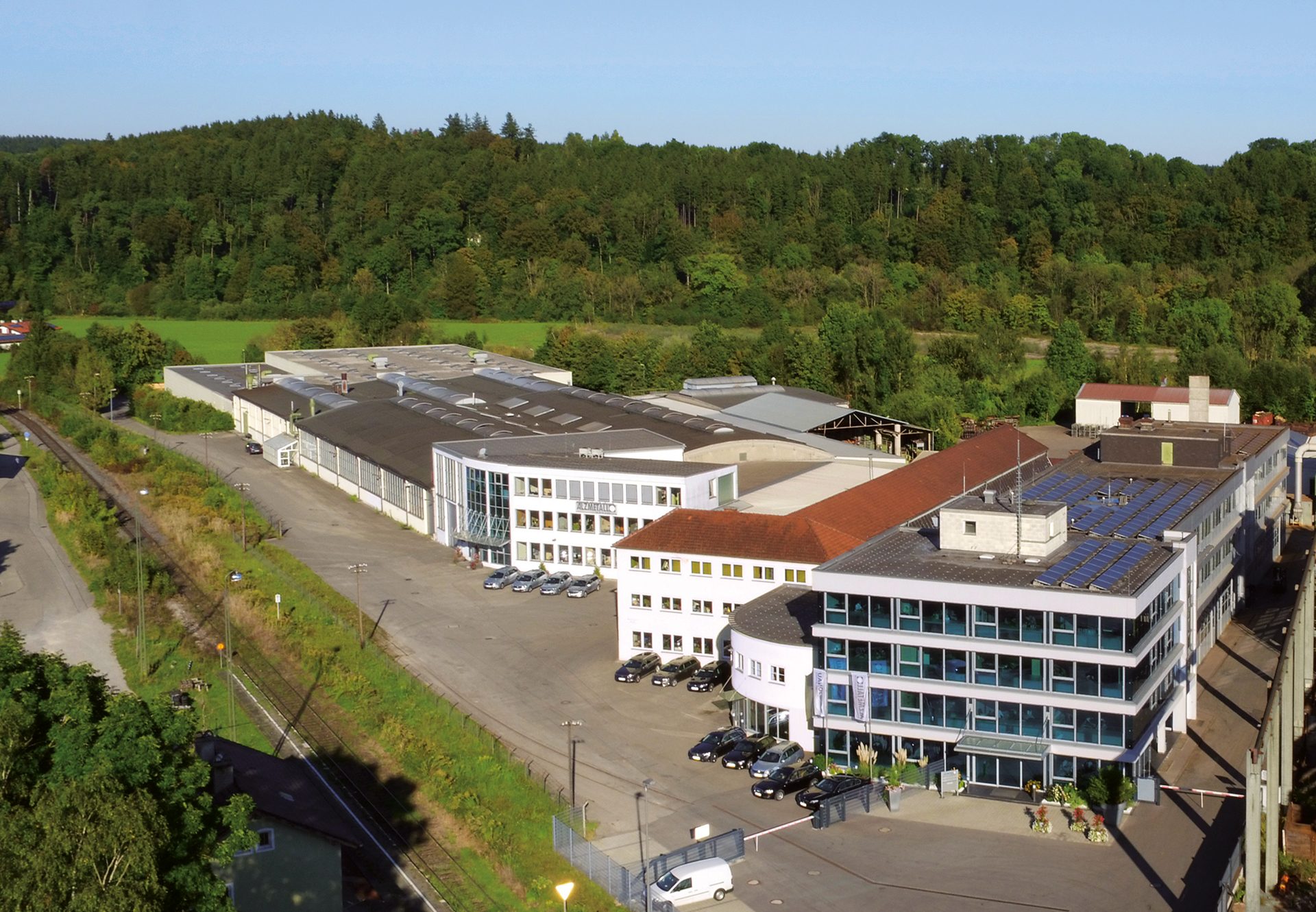 Aerial view of an industrial complex with a railway and forest in the background.