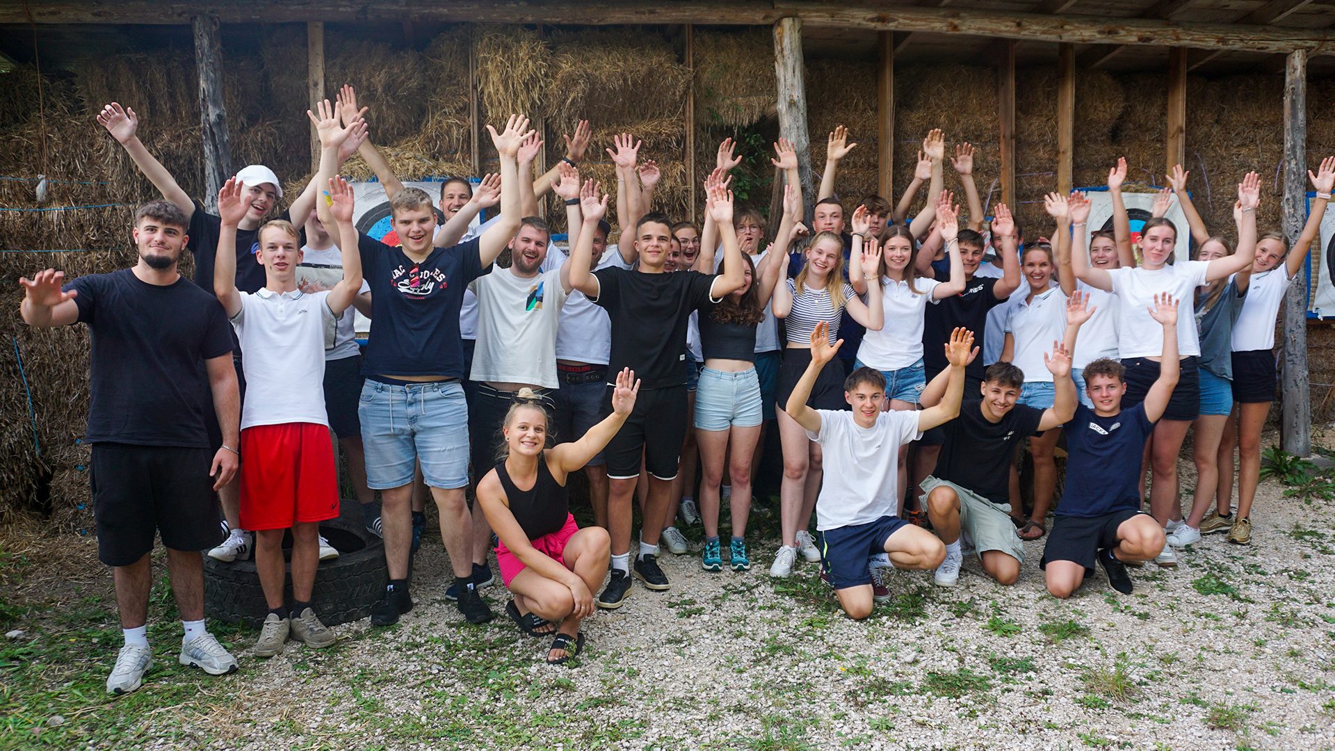 Happy young people raising hands, outdoors with hay bales.