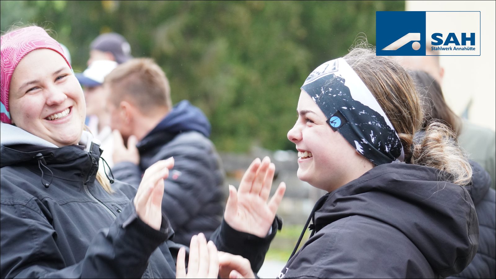 Two smiling women in headbands clapping, with SAH Stahlwerk Annahütte logo.