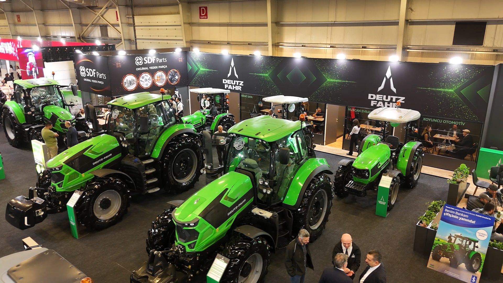 Green Deutz-Fahr tractors on display at an indoor exhibition with people and brand banners.