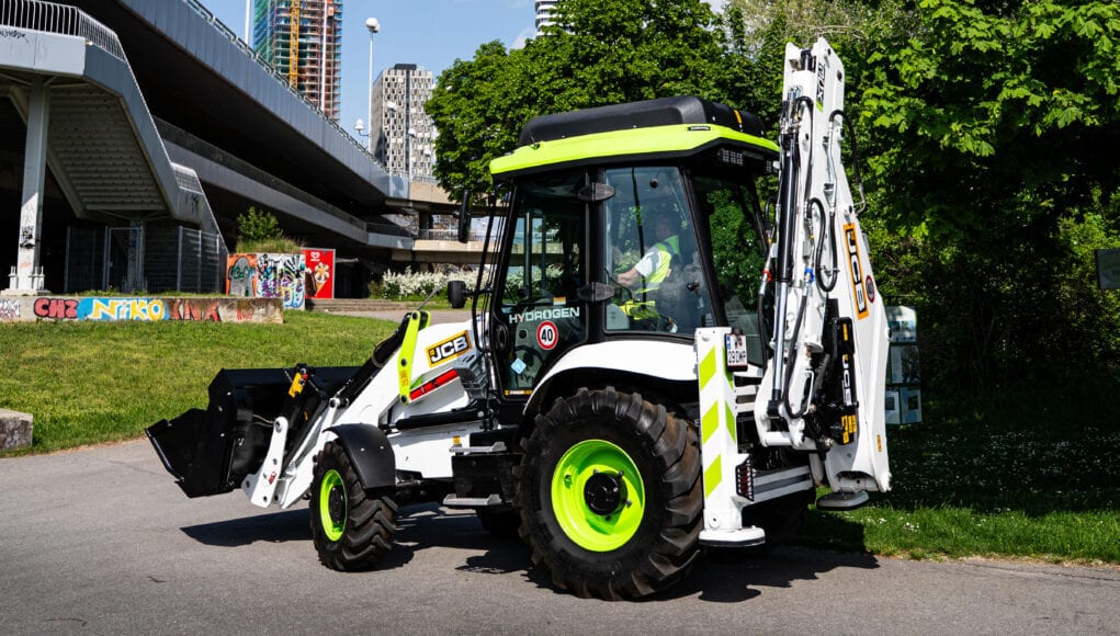 JCB hydrogen backhoe loader in white and bright green on an urban street.