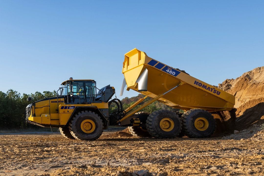 A yellow Komatsu HM 460 articulated dump truck dumping material at a construction site.