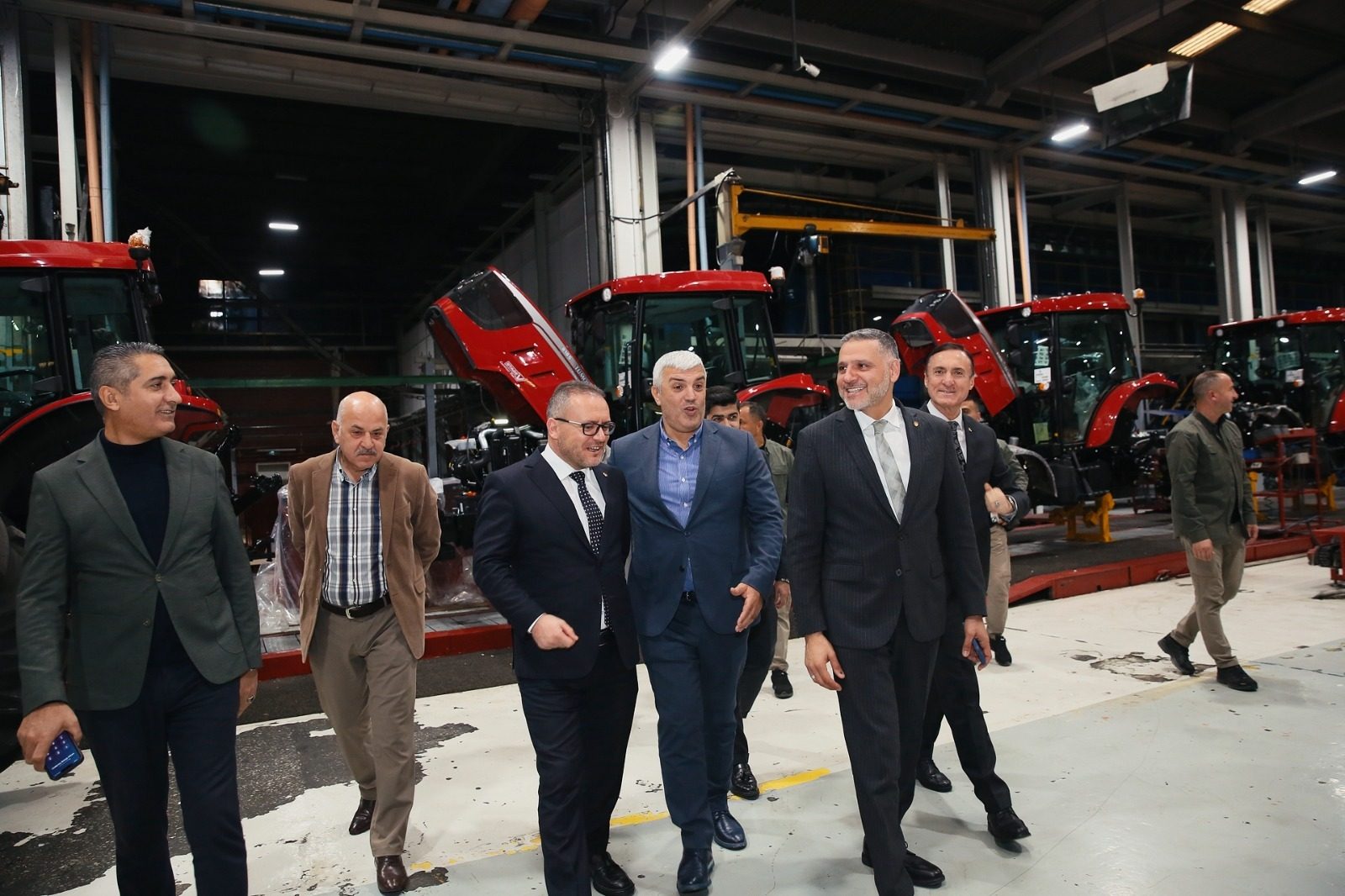 Men in suits walk through a factory with red tractors on an assembly line.