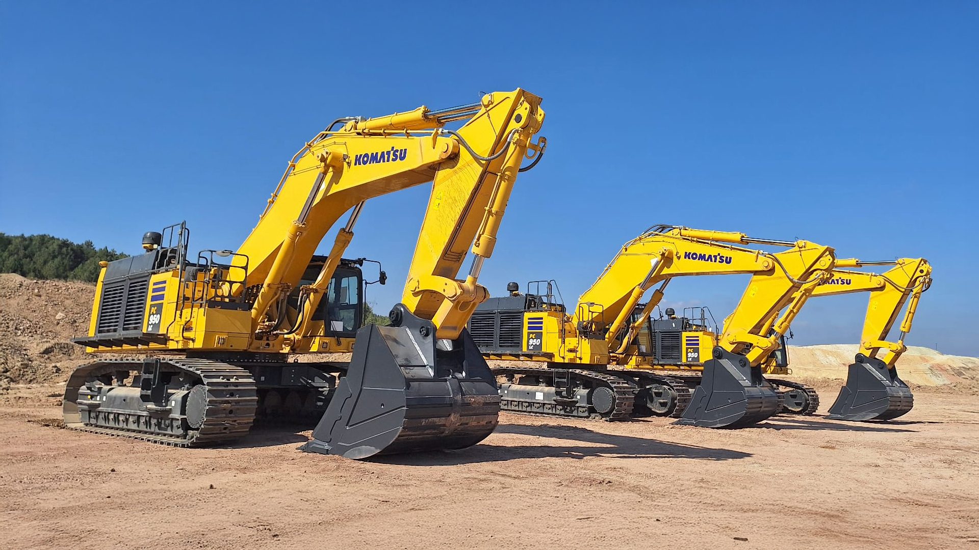 Three yellow Komatsu PC 950 LC excavators on a dirt construction site under a clear blue sky.
