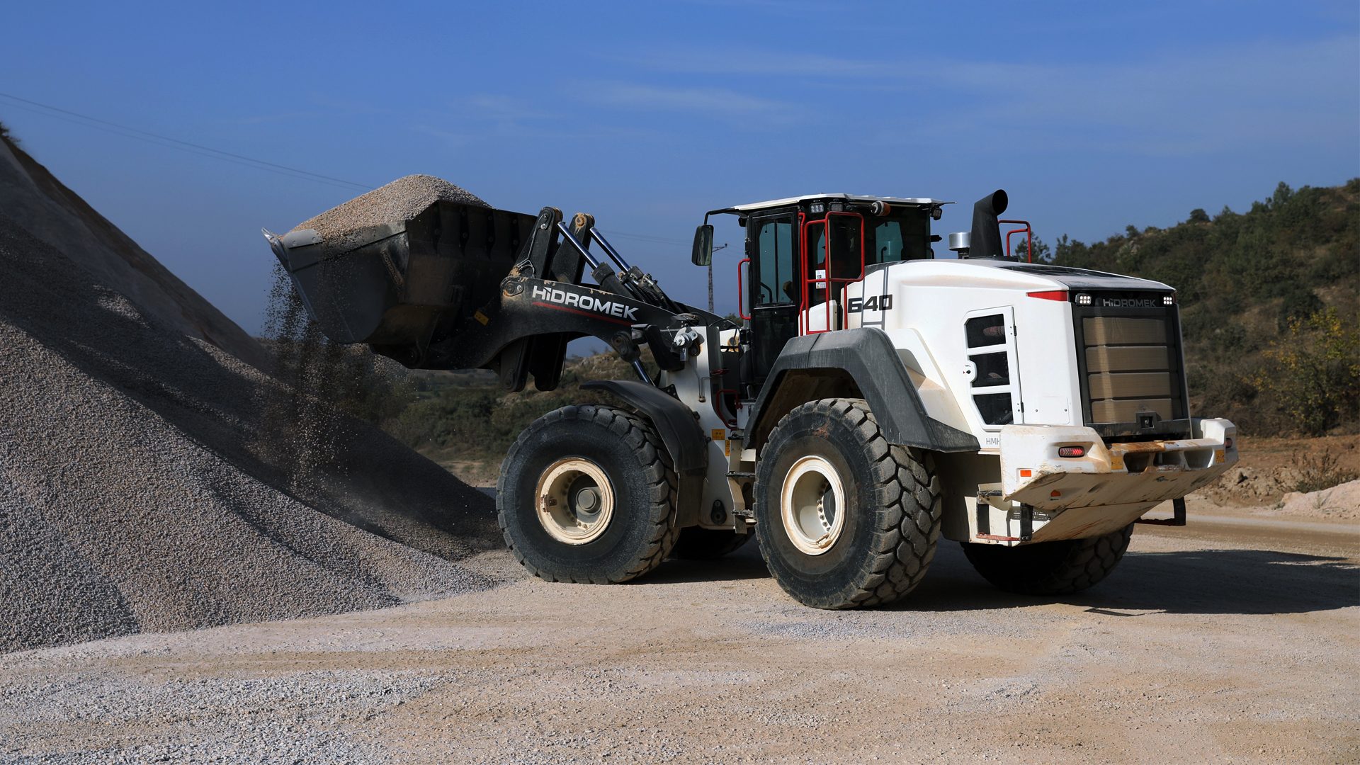 White Hidromek 640 wheel loader actively dumping gravel onto a large pile.