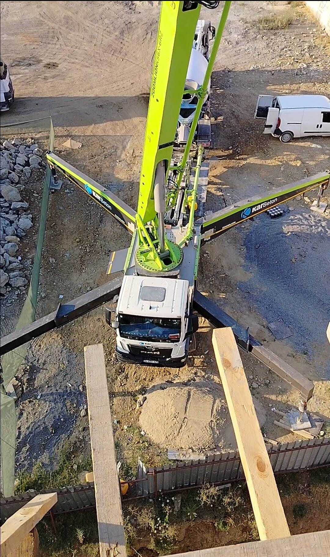 Top-down view of a green concrete pump truck with extended outriggers at a construction site.