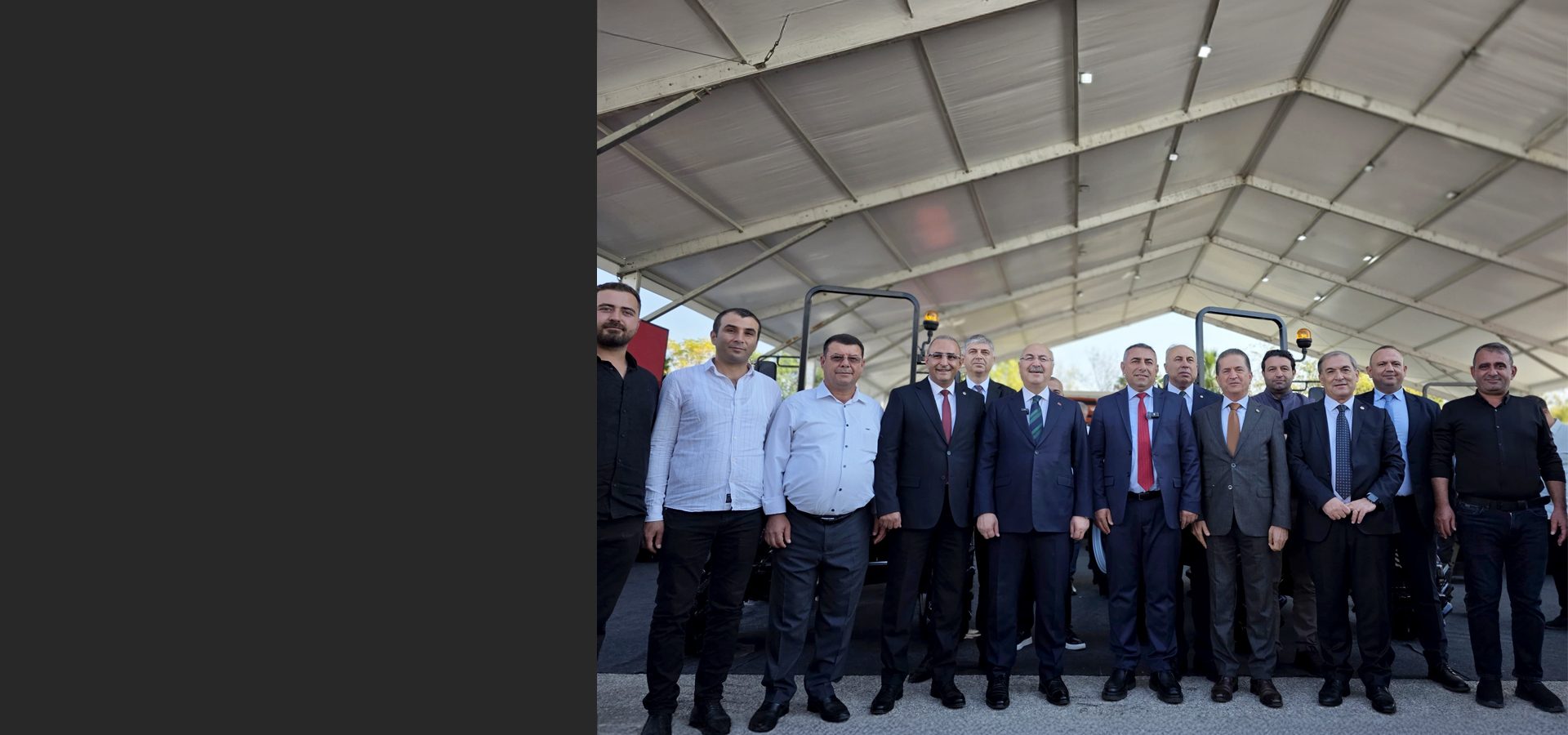 Group of men, mostly in suits, standing under a large tent.