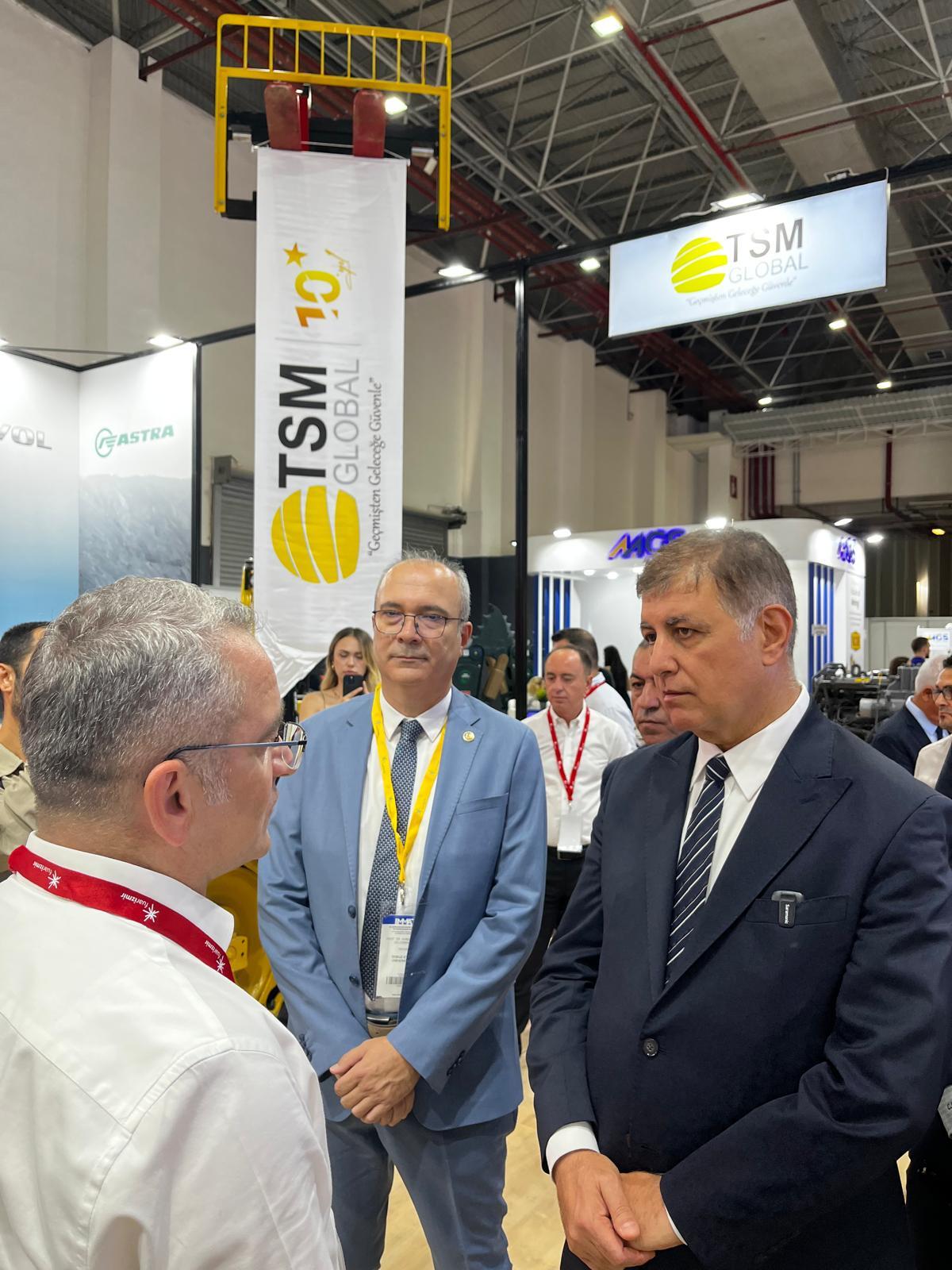 Three men in a convention center, with a "TSM GLOBAL" banner and sign visible.