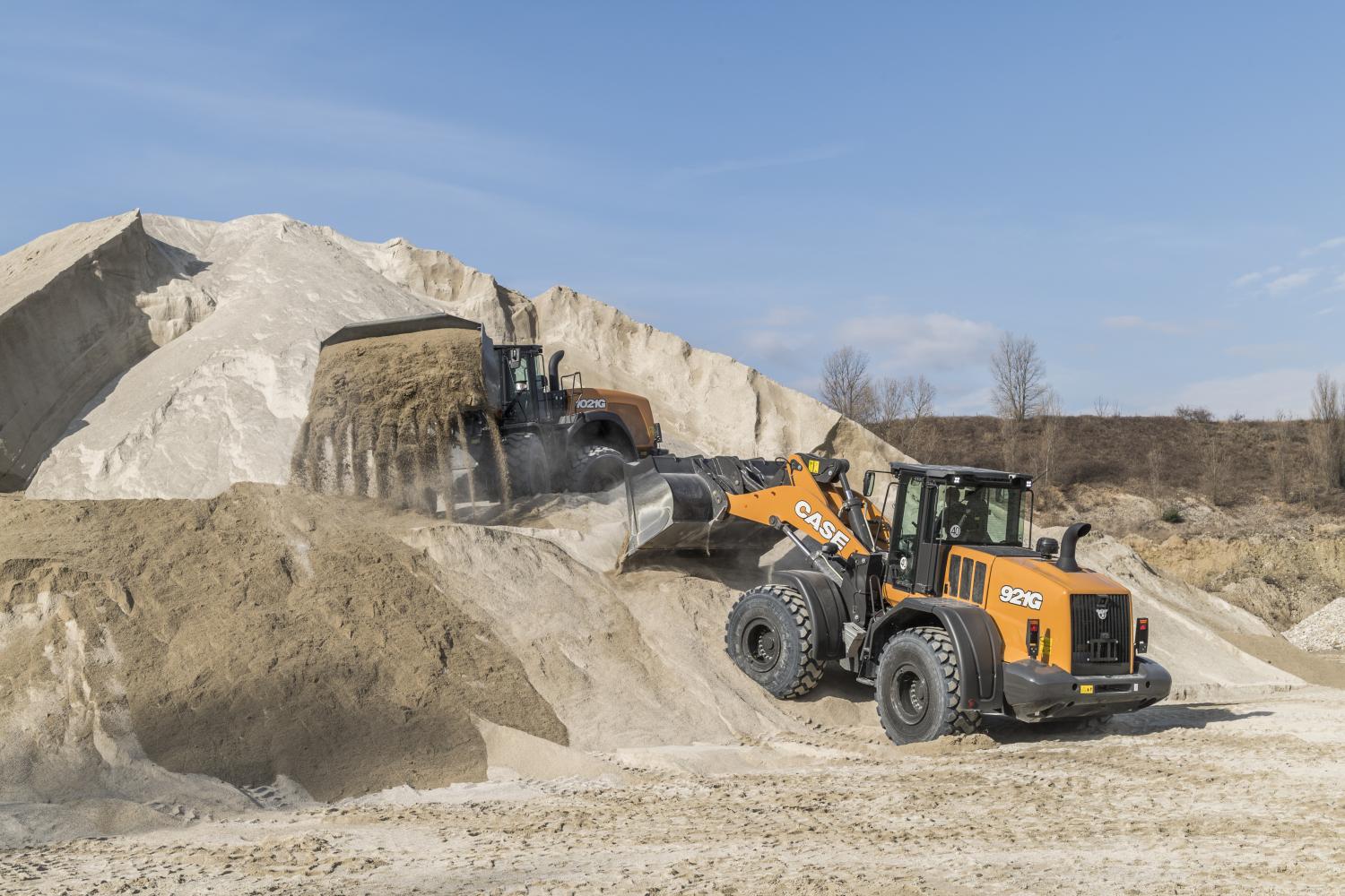 Two orange Case 921G loaders in a sand quarry; one dumps sand from a pile.