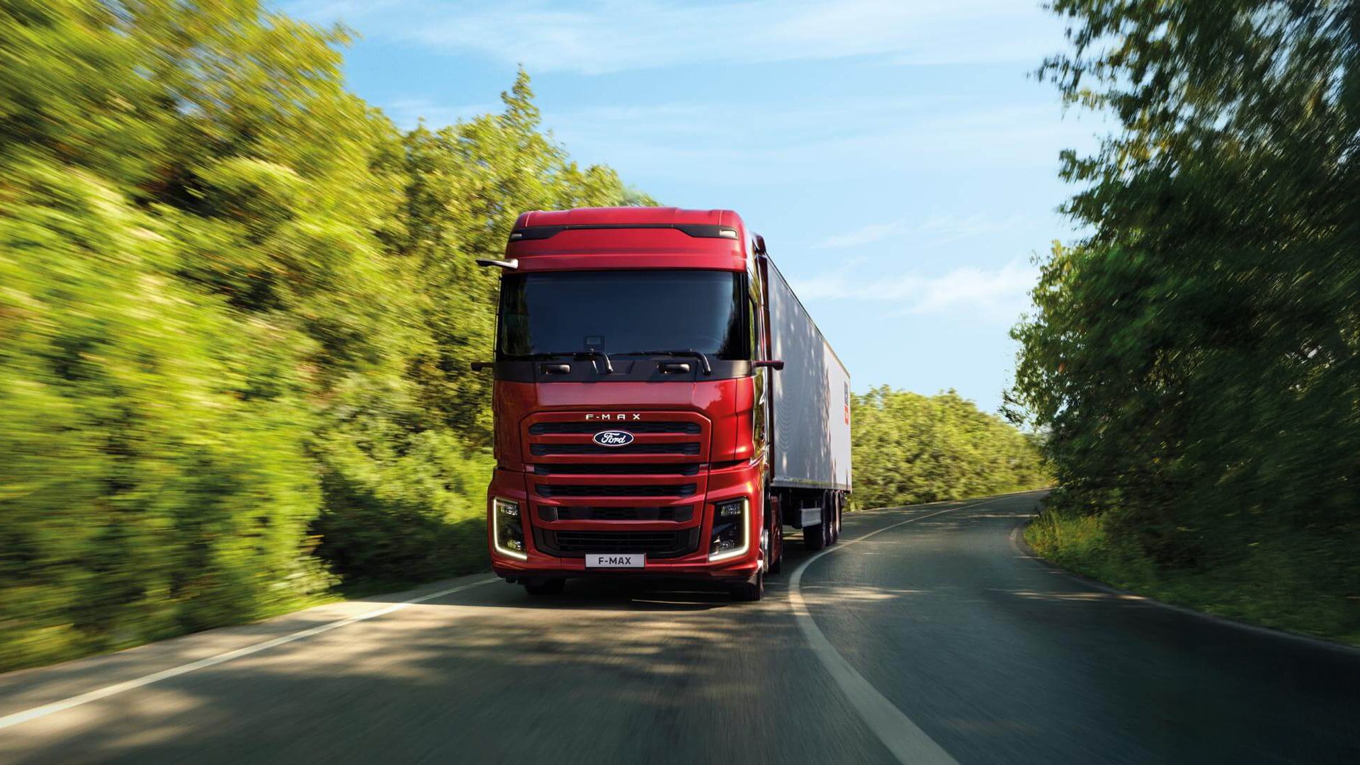 Red Ford F-MAX semi-truck with trailer on a winding road through green trees.