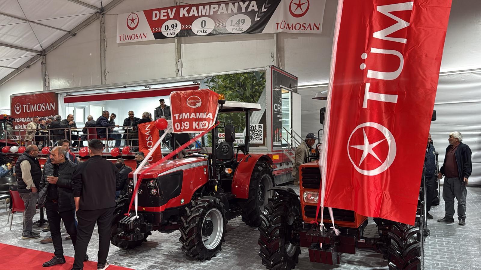 TÜMOSAN event with red tractors, campaign banners, and people gathered indoors.