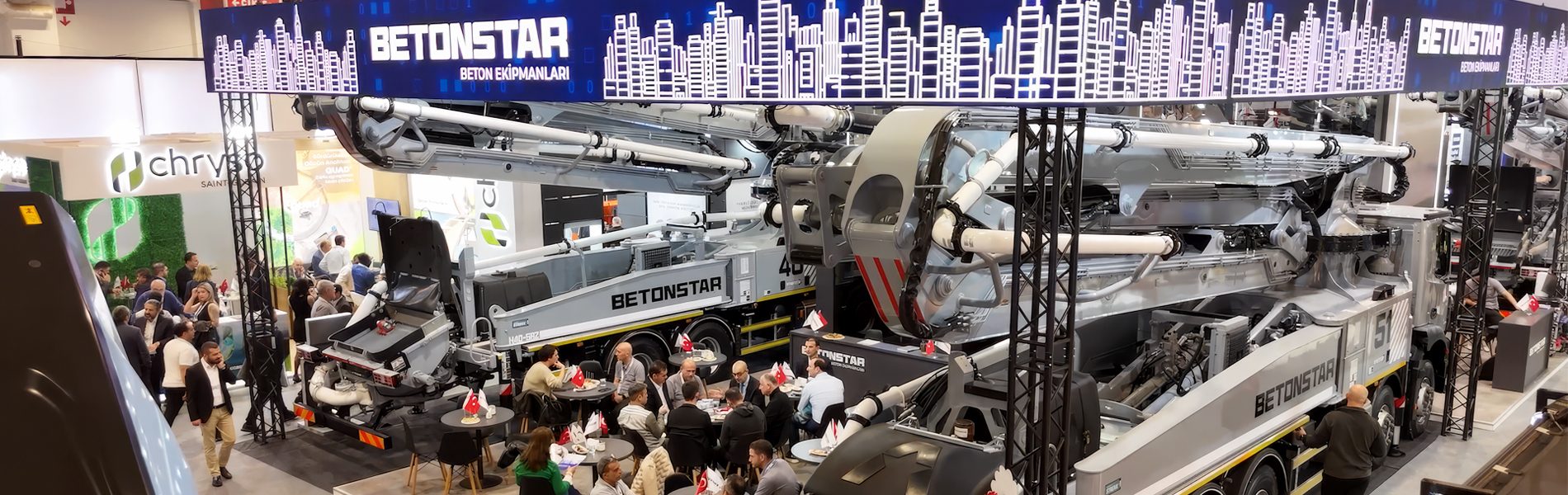 BETONSTAR concrete pump trucks on display at an indoor trade show booth with many people.