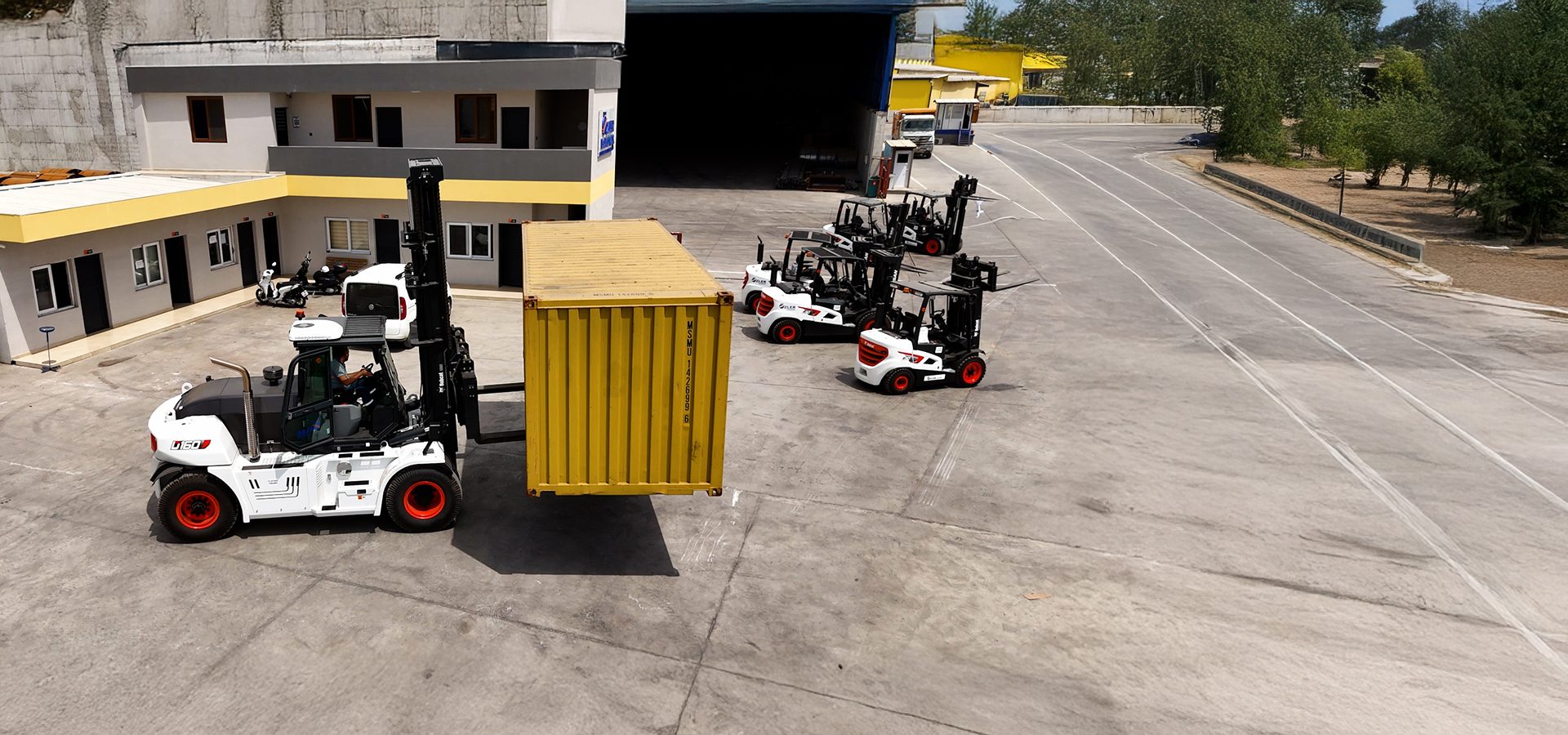 Large forklift lifting a yellow container in an industrial yard.
