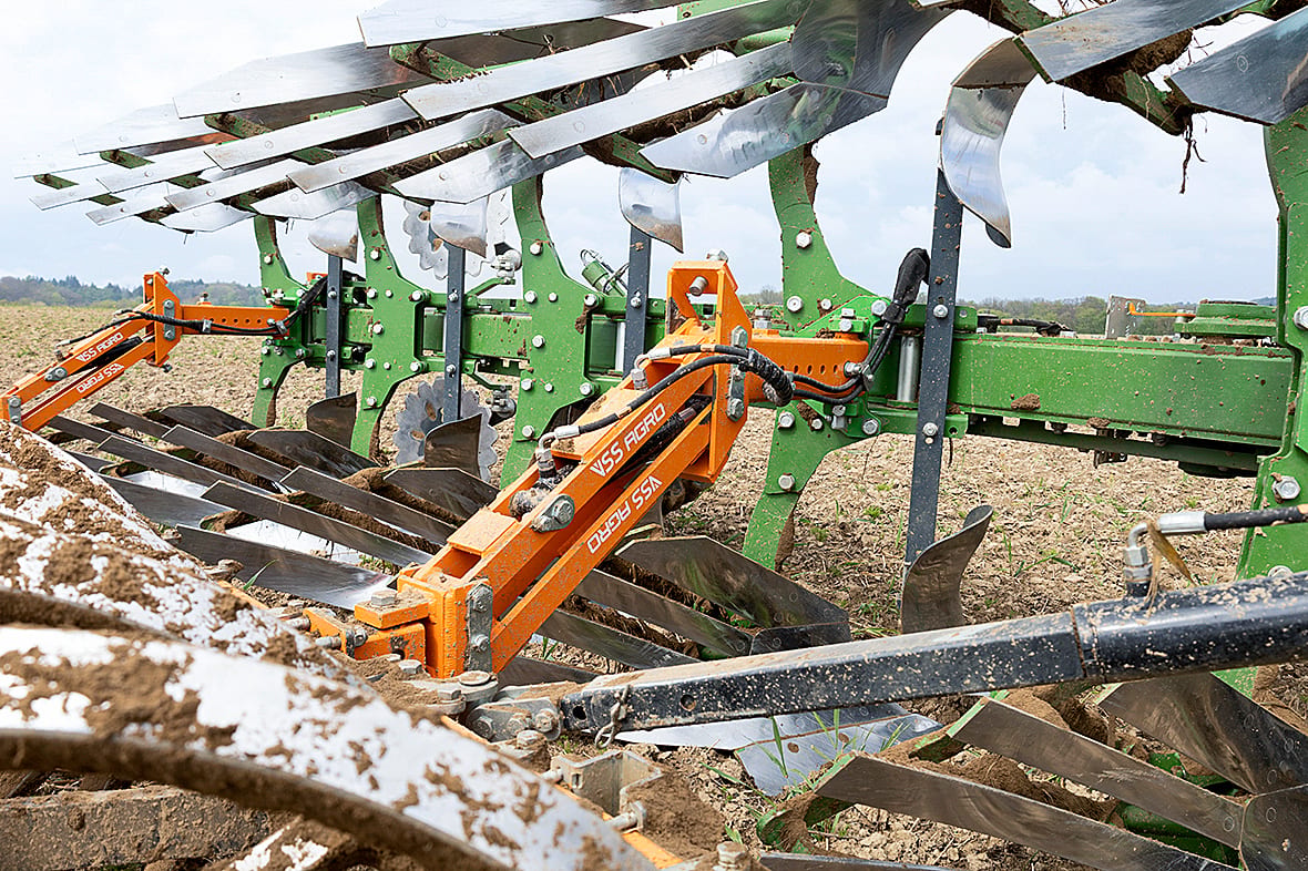 Close-up of a green and orange agricultural plow turning soil in a field.
