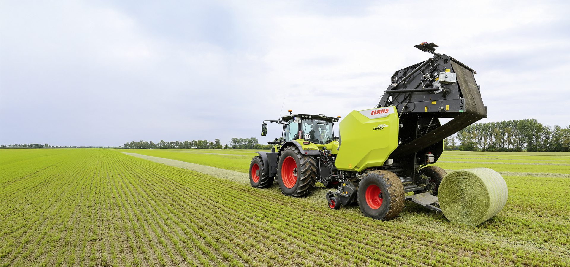 Tractor with baler creating a round bale in a green crop field.