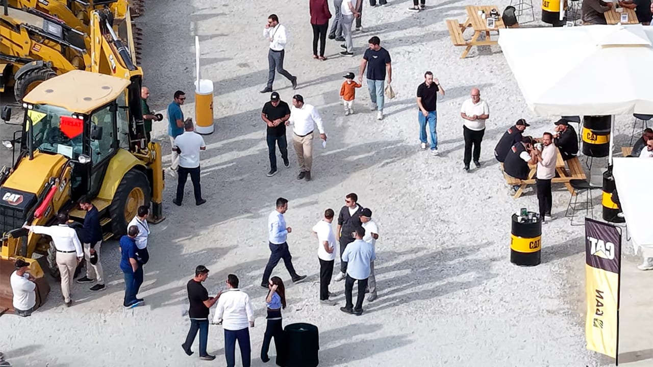 People gathered around yellow Caterpillar construction vehicles at an outdoor exhibition.