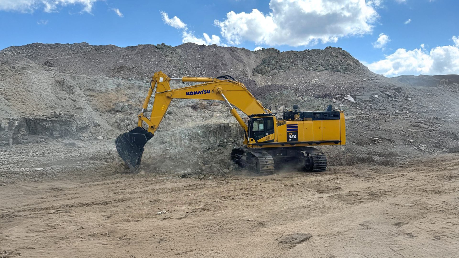 Yellow Komatsu PC 950 LC excavator working in a rocky quarry under a cloudy sky.