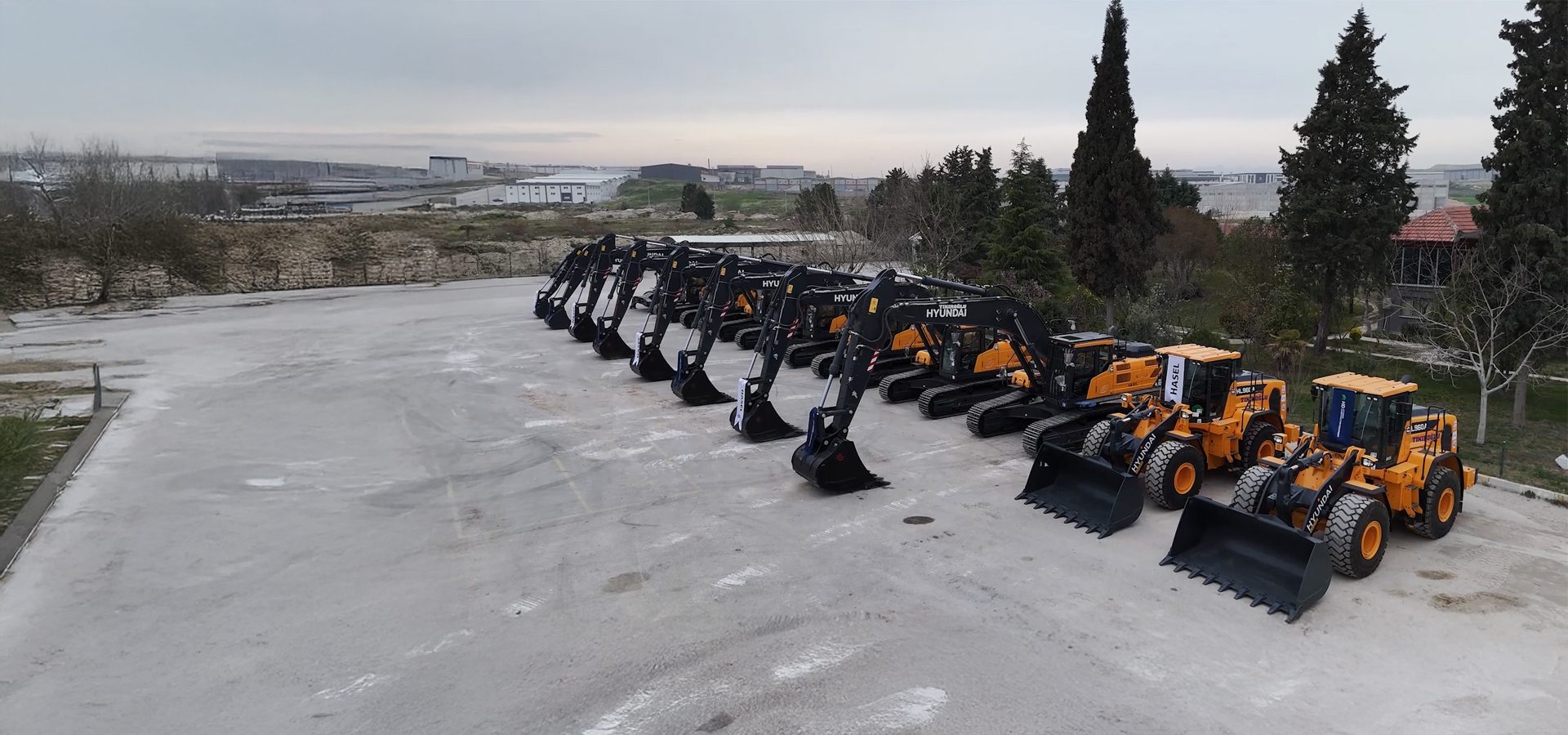 A fleet of new black and yellow Hyundai excavators and wheel loaders lined up on a paved lot.