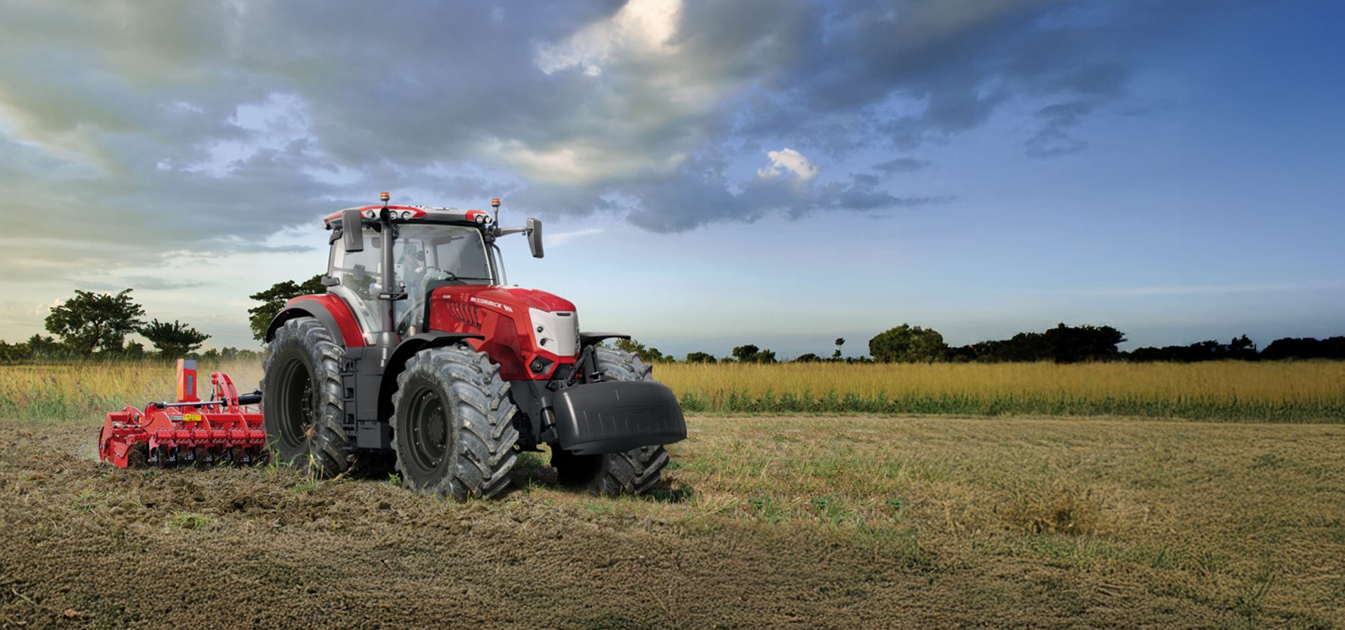 A red McCormick tractor tilling a field under a cloudy sky.