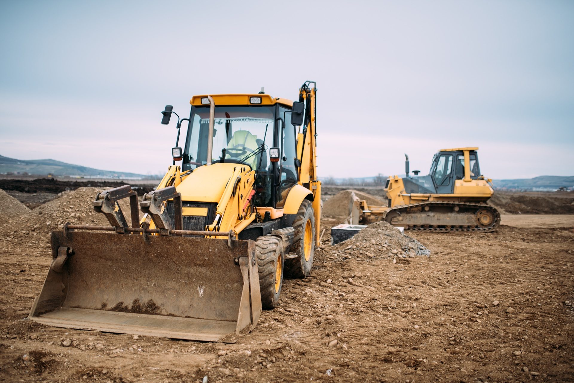 Yellow backhoe loader and bulldozer on a dirt construction site.