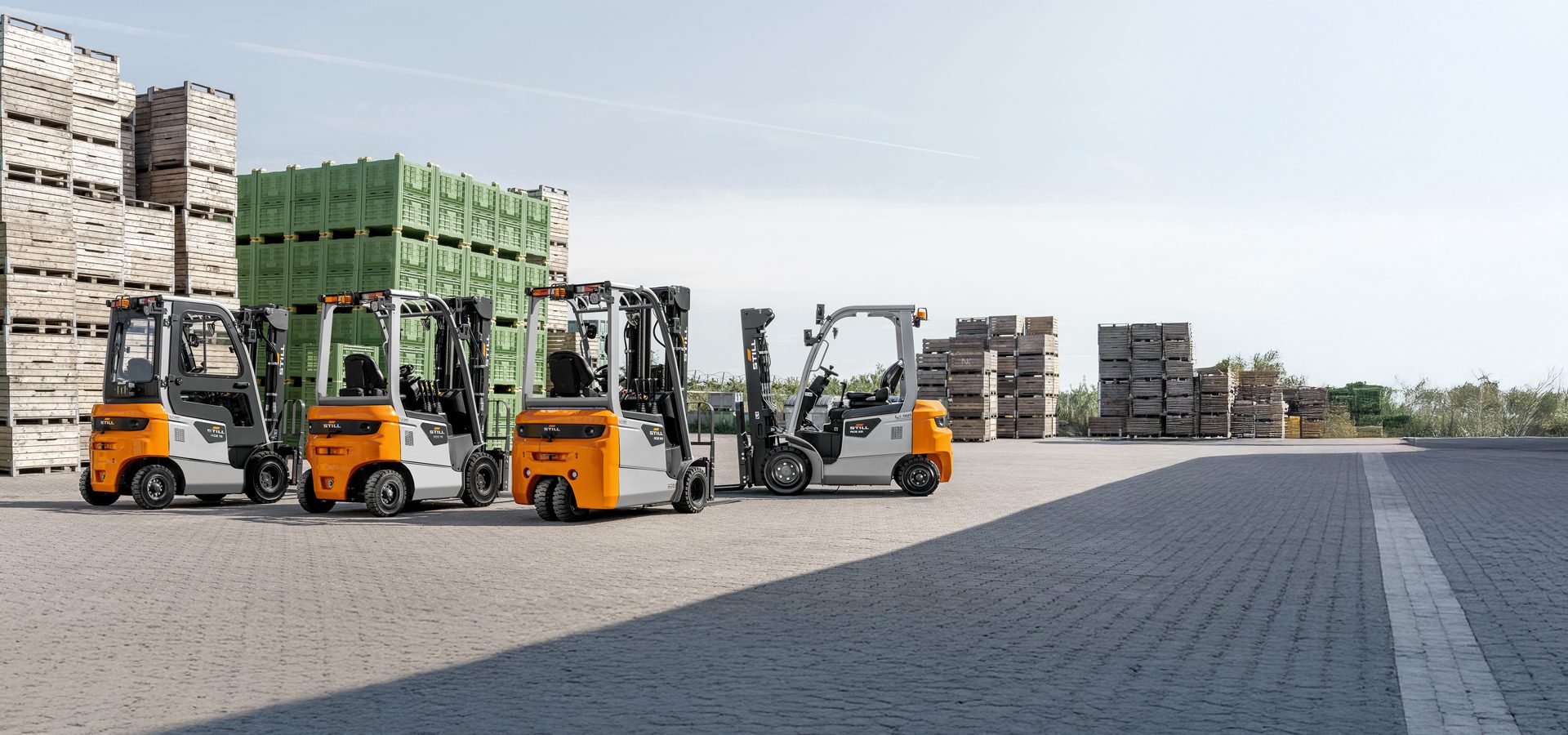 Four forklifts parked near wooden and green plastic crates outdoors.