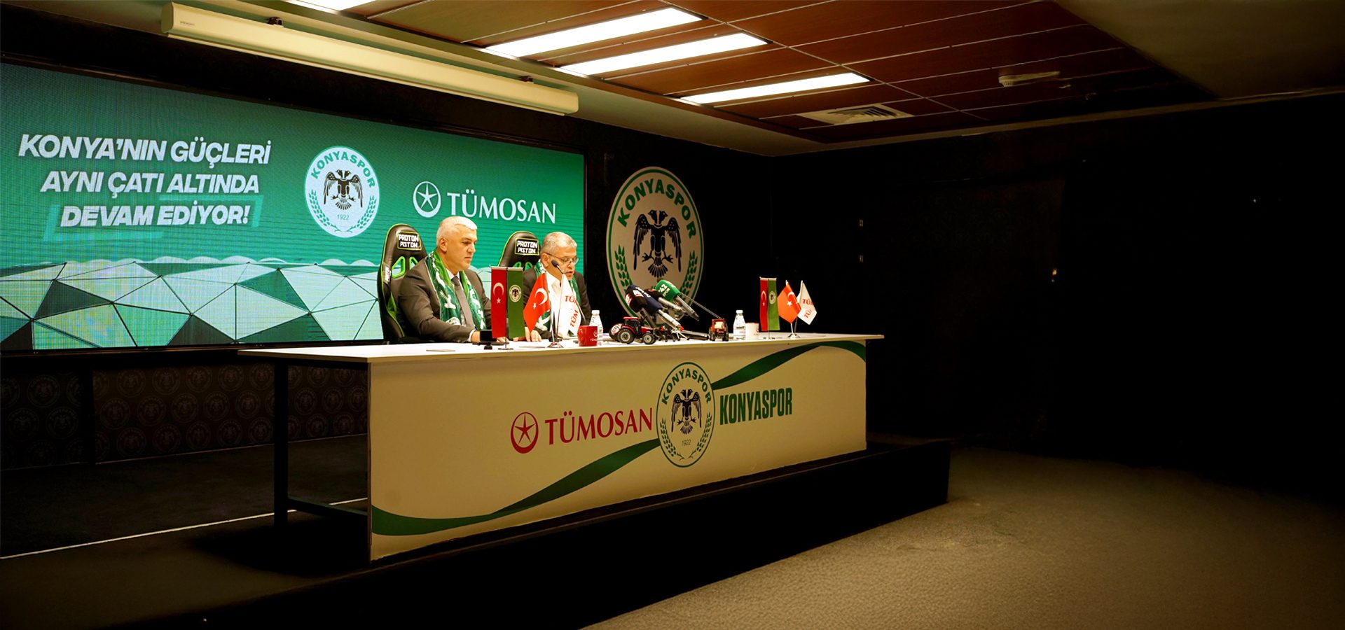 Press conference with two men at a table featuring Konyaspor and Tümosan logos, flags, and microphones.