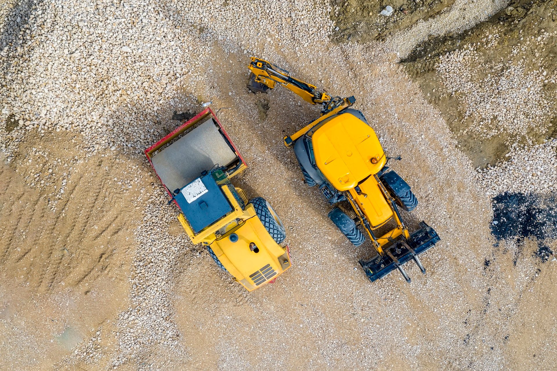 Aerial view of heavy machinery, an excavator loading a dump truck with gravel at a construction site.