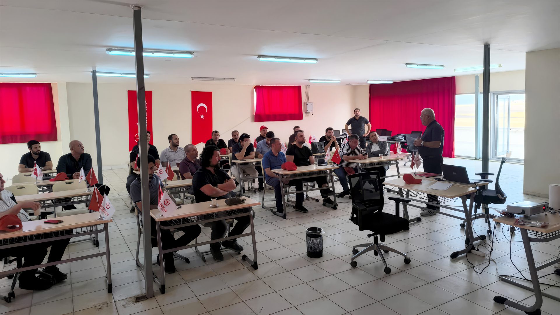 Men gathered in a room with a speaker, Turkish flags, and branded flags on desks.
