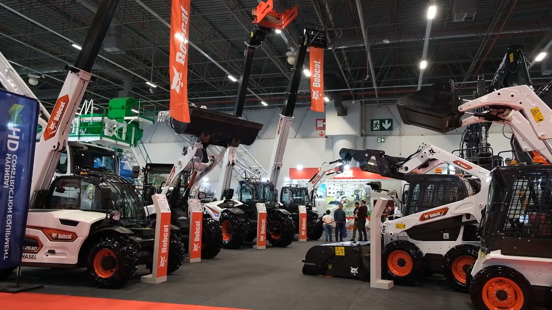 A wide shot of an indoor exhibition hall featuring numerous Bobcat telehandlers and skid steers on display.