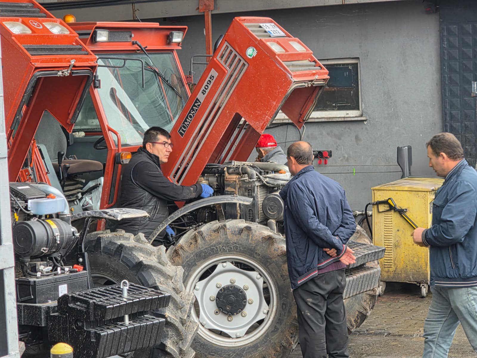 Mechanics are fixing a red tractor with its hood open.