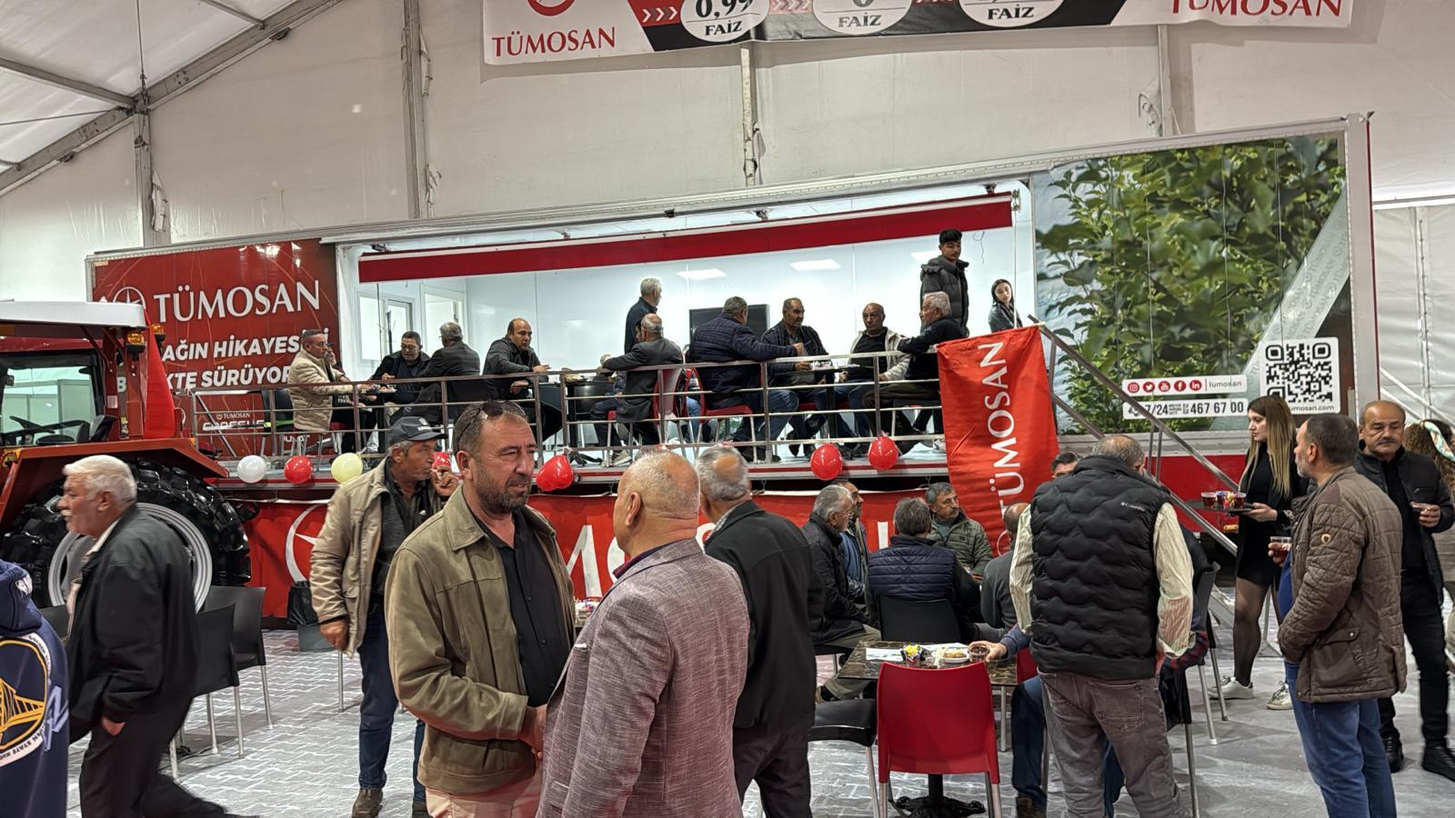 Men mingle at a TÜMOSAN event with a tractor display and branding.