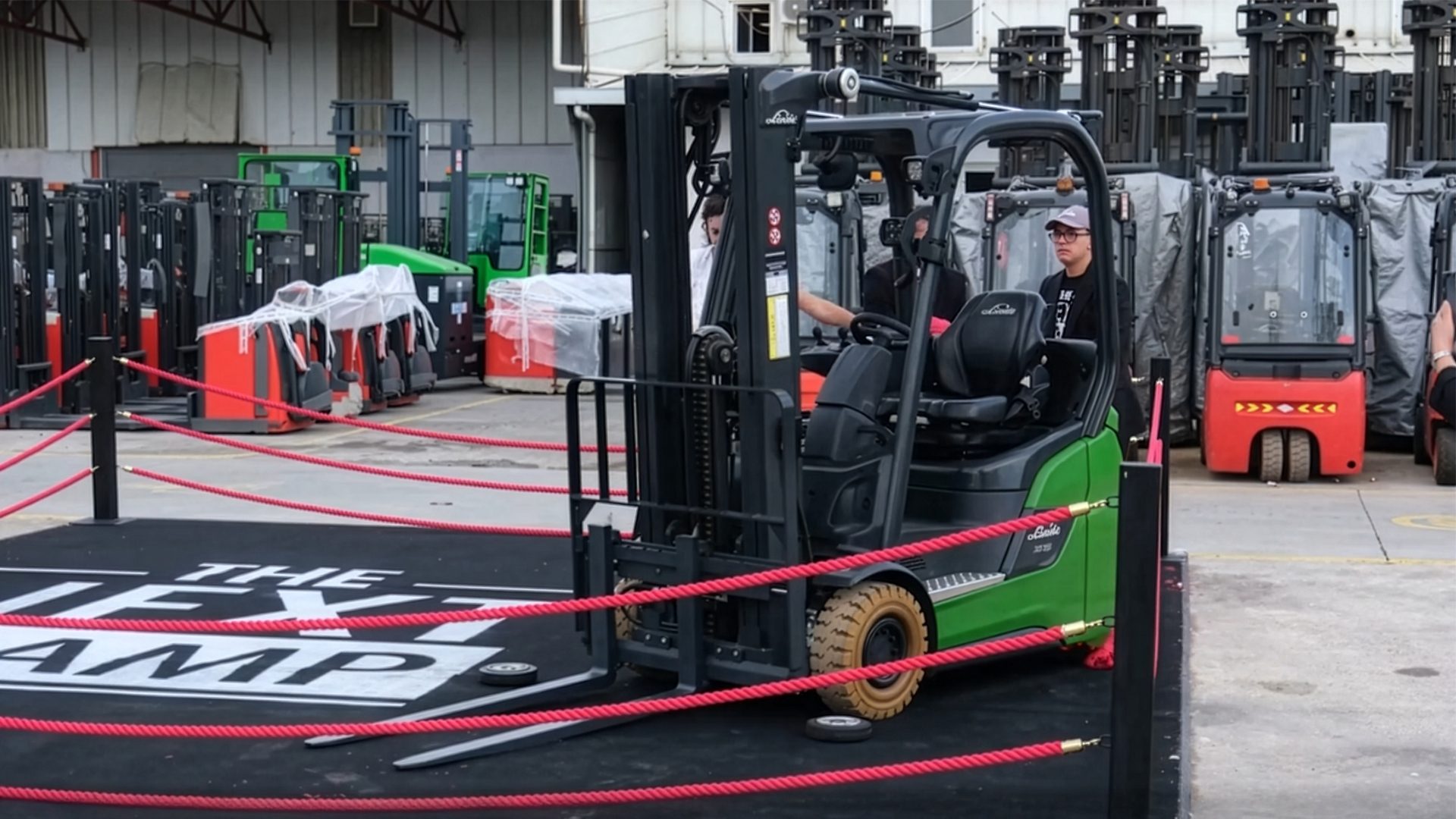 A green forklift with an operator in a roped-off area, surrounded by many other forklifts.