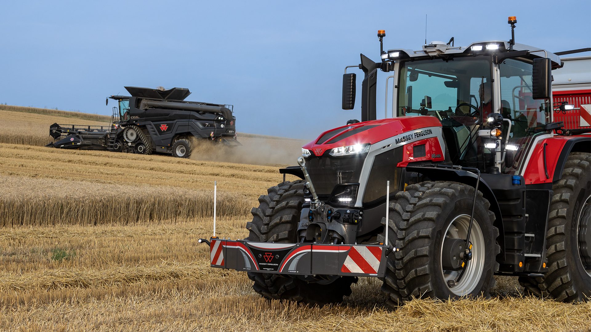 Red tractor and black combine harvester working in a golden, harvested field.