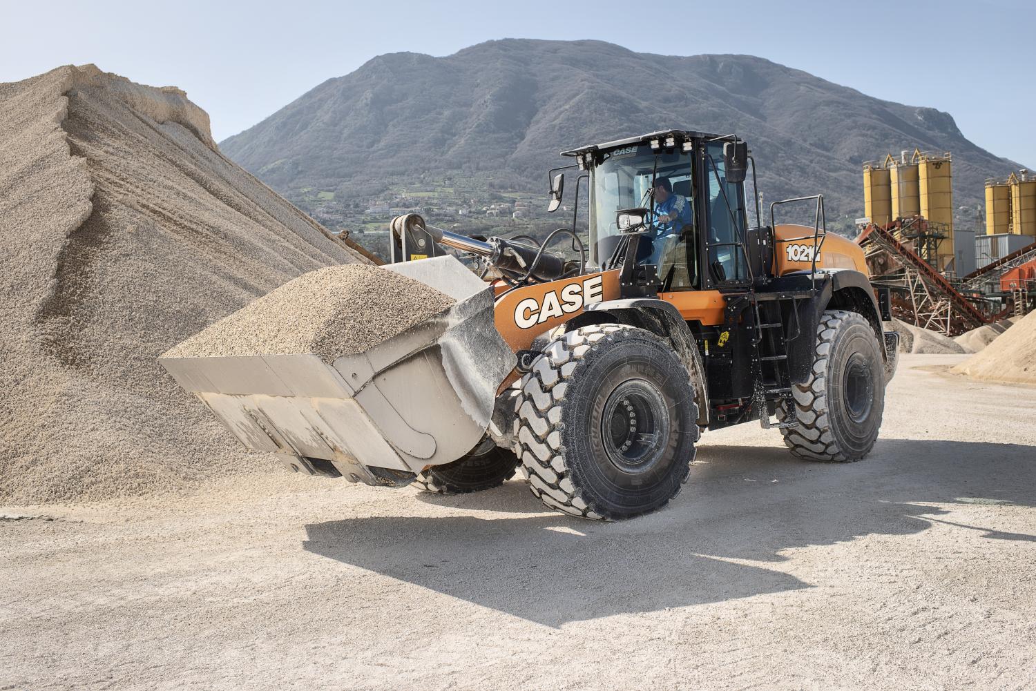 Orange CASE 1021 wheel loader with a driver scooping gravel from a large pile.