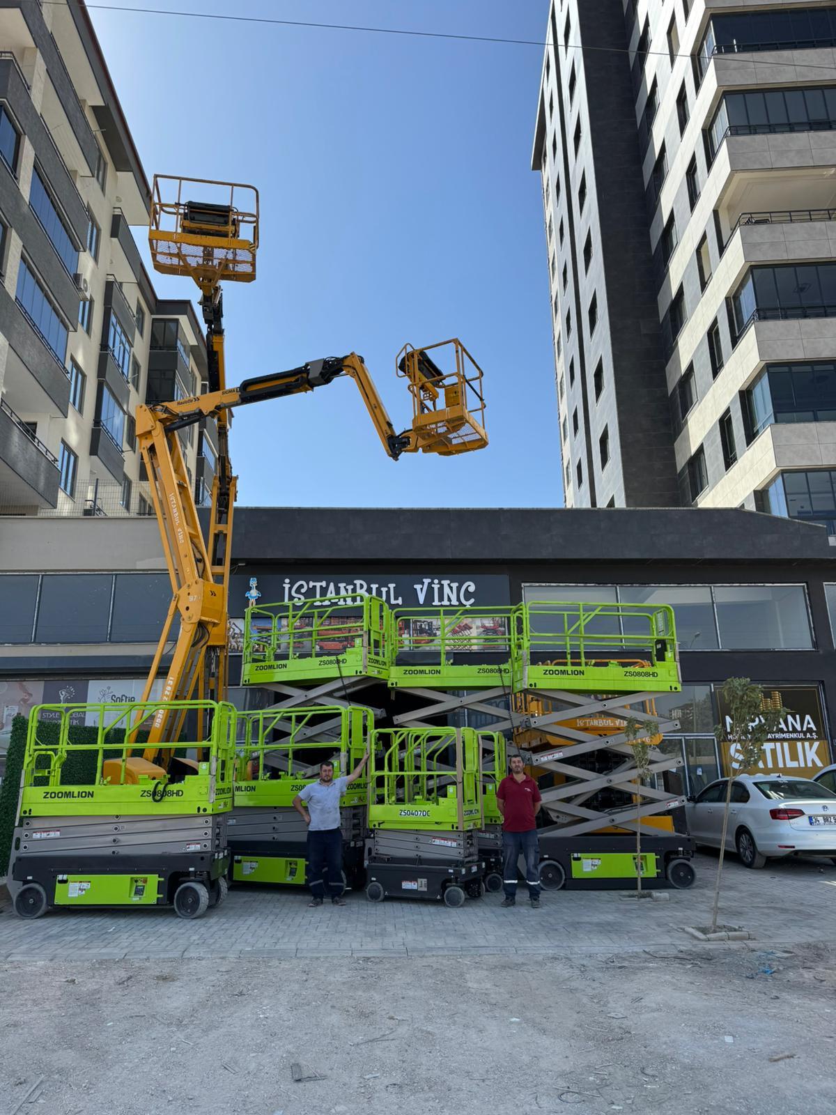 Two men with green Zoomlion scissor lifts and a yellow boom lift outside 'ISTANBUL VINC' building.