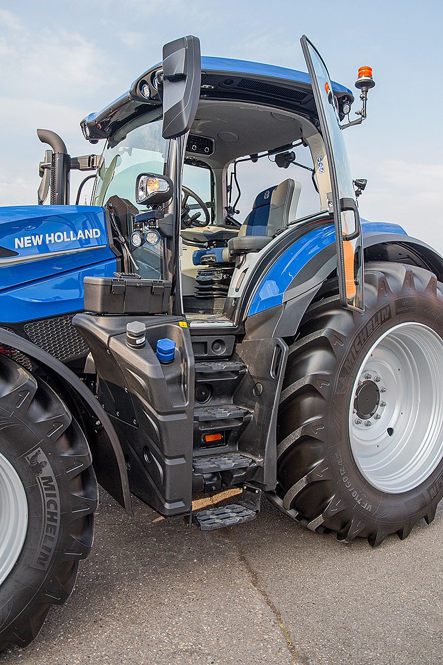 Side view of a blue New Holland tractor, featuring its open cabin door, steps, and large wheels.