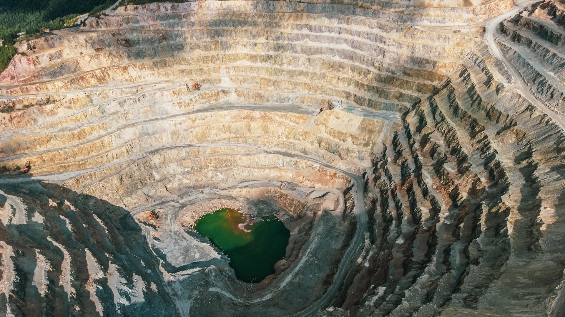 Aerial view of a large, terraced open-pit mine with a vibrant green lake at its deepest point.