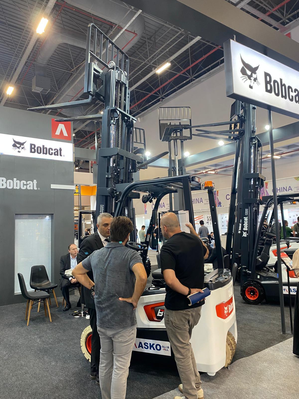 Men discussing Bobcat forklifts at a trade show booth.